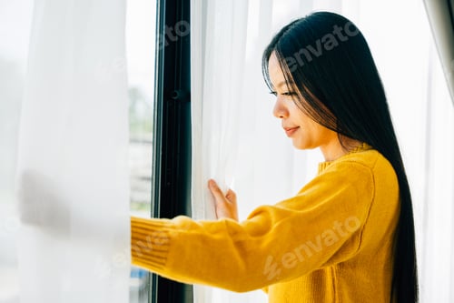 Preview: A young woman opens curtains in the early morning smiles at the view feeling relaxed
