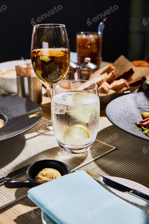 Preview: water with ice and lemon near glass of white wine on table in restaurant