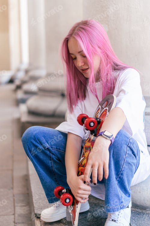 Preview: Teenage girl with pink hair and a skateboard on a summer day against the background of city building