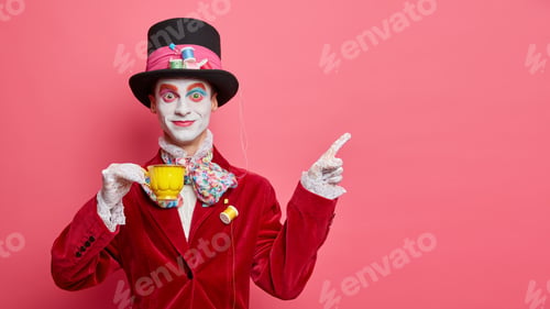 Preview: Smiling glad hatter in fashionable costume has aristocratic manners drinks tea and indicates at copy