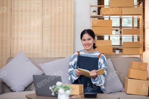 Preview: young female entrepreneur writes on the front of a product box to sell products online and prepares