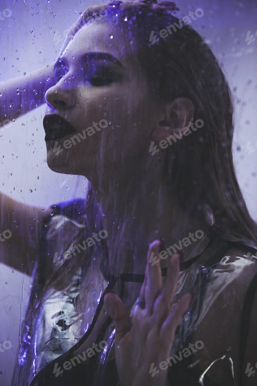 Preview: Fashionable model with wet hair dressed in black swimming suit and transparent rain coat is posing