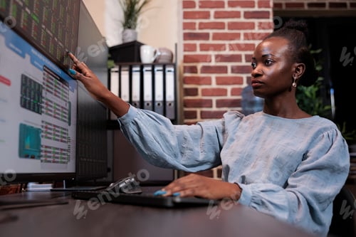 Preview: Brokerage agent analyzing real time financial data charts while using multi monitor workstation.