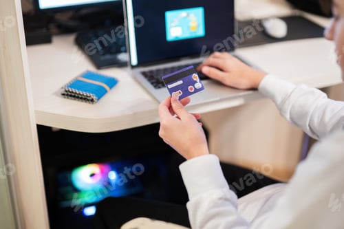 Preview: Happy teenage boy using laptop and credit card, sitting at desk and ordering goods online from home.