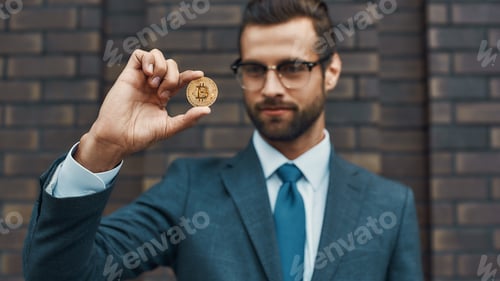 Preview: Digital currency. Handsome businessman in formal wear and eyeglasses holding bitcoin in one hand and
