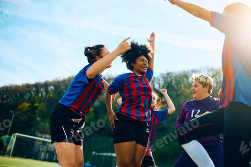 Preview: Black soccer player and her teammates celebrating after winning the match at the stadium.