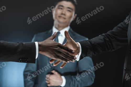 Preview: selective focus of multiethnic business partners shaking hands with asian colleague standing near by