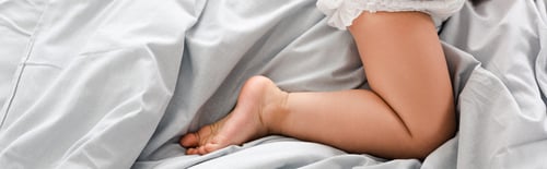 Preview: Panoramic shot of cute barefoot baby leg on white sheets
