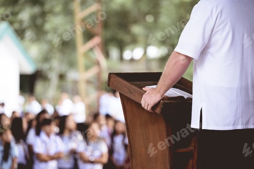 Preview: Closeup shot of a male standing near a wooden stand reading the bible for children