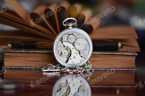 Preview: Old books and mechanism of old pocket watch on a reflective surface