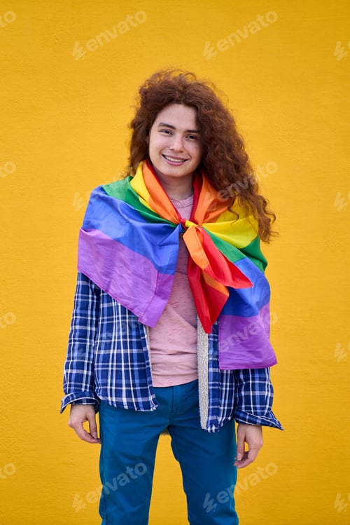 Preview: Portrait smiling redhead non-binary person rainbow flag on shoulders looking at camera isolated.