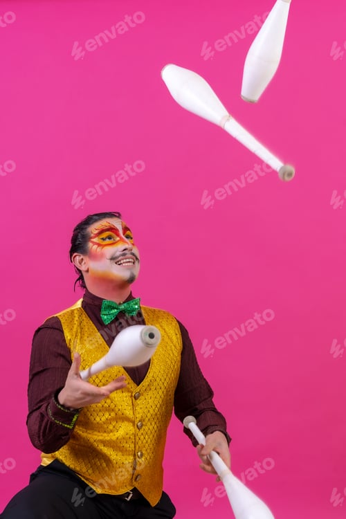 Preview: Clown with white facial makeup on a pink background, smiling juggling maces