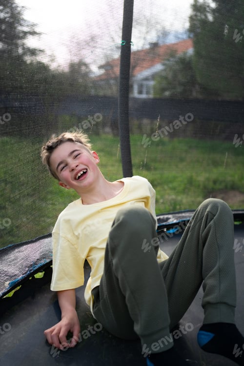 Preview: Cheerful boy laughing on trampoline in backyard