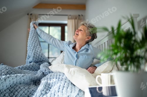 Preview: Senior woman in bed at home getting up in the morning, stretching