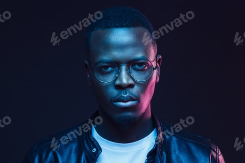 Preview: Serious African man wearing glasses and leather jacket at night