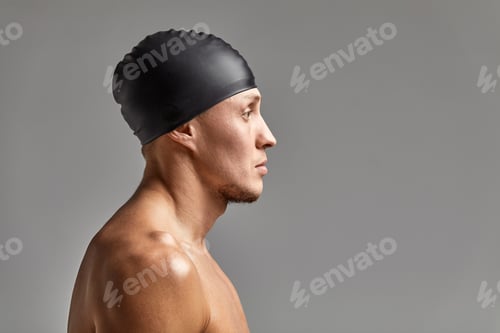 Preview: portrait of a young man swimmer wearing a rubber hat, standing against a gray background hat getting