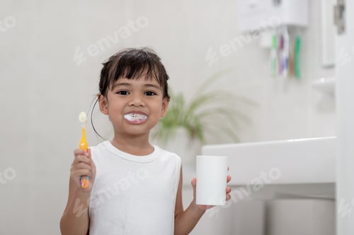 Preview: Little cute baby girl cleaning her teeth with a toothbrush in the bathroom