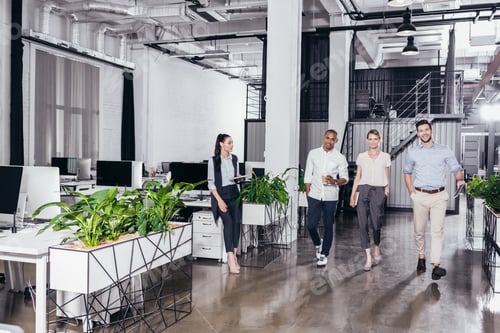 Preview: smiling young multiethnic business colleagues walking together in office