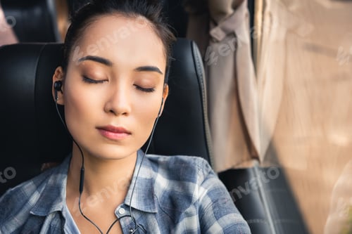 Preview: portrait of asian woman sleeping and listening music in earphones during trip on travel bus