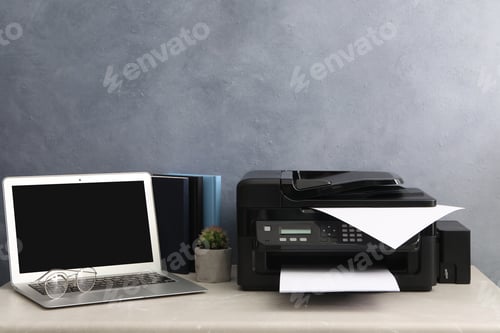 Preview: New modern printer and laptop on grey table at workplace
