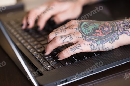 Preview: Tattooed hands typing on a laptop