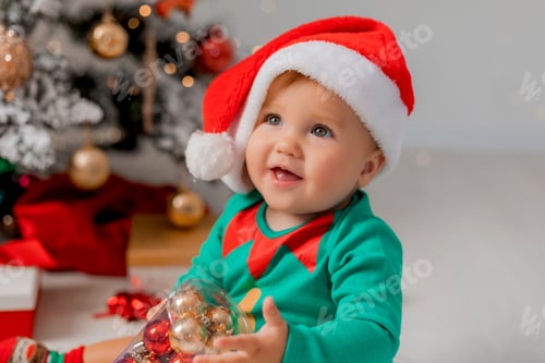 Preview: Santa's little helper next to the Christmas tree with Christmas balls in his hands. portrait of baby