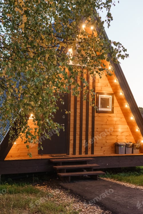 Preview: The concept of glamping and renting a chalet for weekend. Wooden house with a veranda in nature
