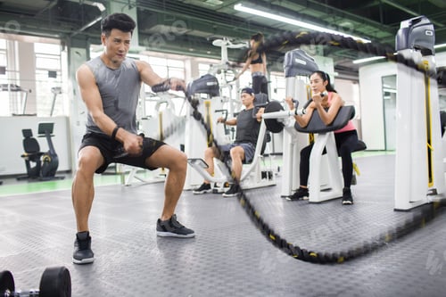 Preview: Young man exercising with battling rope at gym