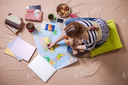 Preview: Young woman making marks on the map while sitting on the floor
