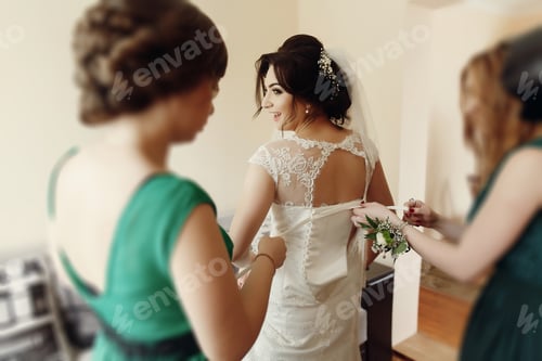 Preview: Stylish beautiful bridesmaids helping gorgeous brunette bride in white dress