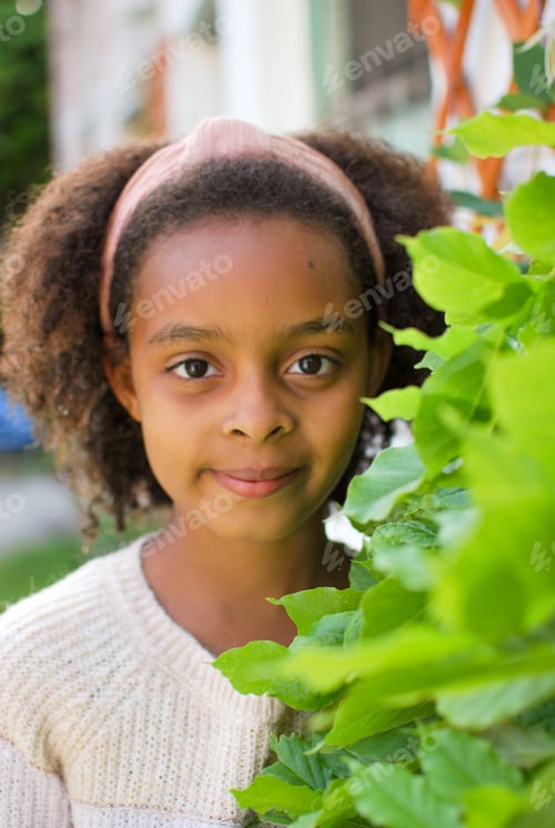 Preview: Portrait of a girl of mixed origine with curly hair and headband in between green leaves - smile