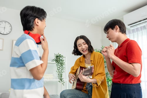 Preview: Diverse Asian friends playing guitar and dancing in living room at home.