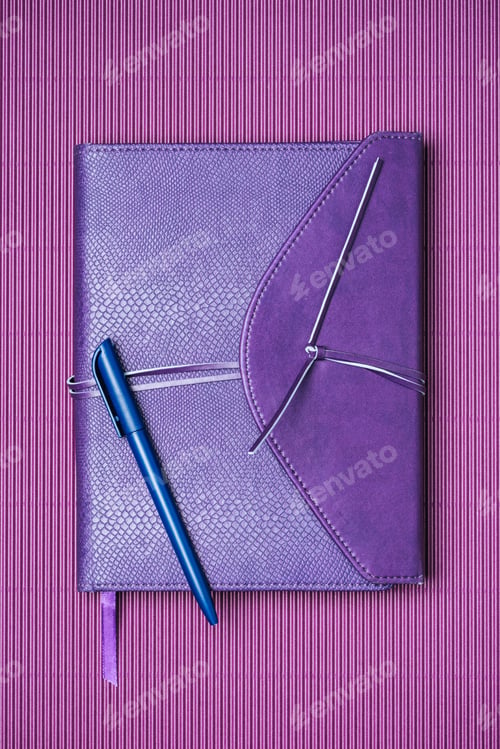 Preview: top view of blue pen and notebook on purple background