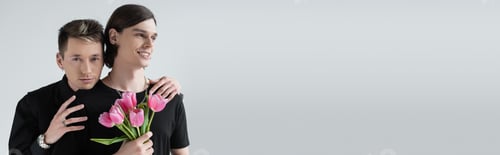 Preview: Young gay man embracing boyfriend with pink tulips isolated on grey, banner