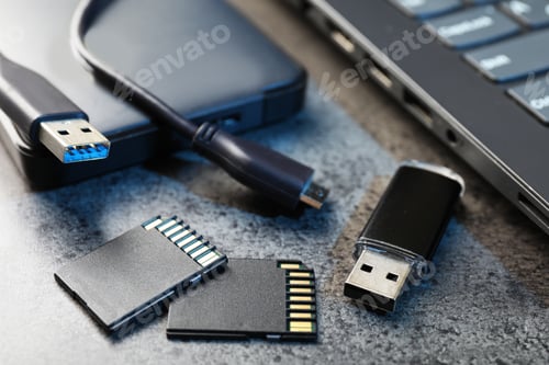 Preview: SD memory cards, USB flash drive, hard disk drive with cable and laptop on dark grey table, closeup