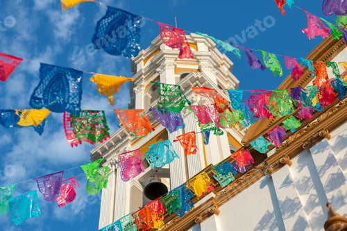 Preview: Festive garland of colorful papel picado hanging above a church bell tower.