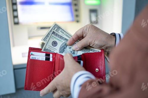 Preview: Woman hand puts many dollars in wallet near ATM outdoor. Modern technology, banking money