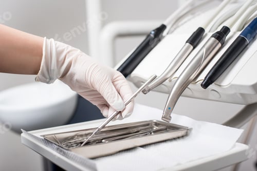 Preview: Dentist with gloved hand is picking dental tool in dental office