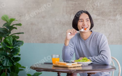 Preview: Portrait of happy handsome asian man eating breakfast in a cafe hotel