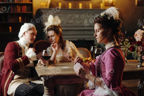 Preview: Caucasian Young Adults Playing Cards in Baroque Renaissance Setting Indoors