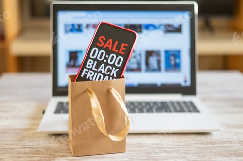 Preview: Smartphone in shopping bag shows Black Friday countdown with laptop, highlighting online deals.