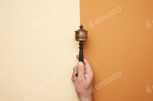 Preview: Copper prayer drum on a stick in a male hand on a brown background