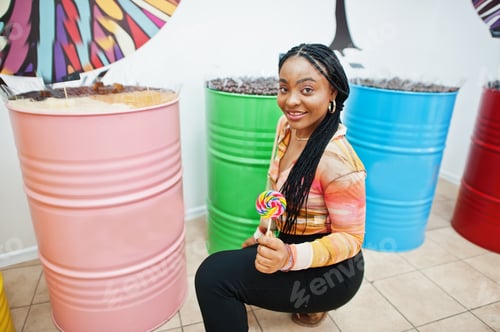 Preview: African american millennial lady at candy shop with lolipops.
