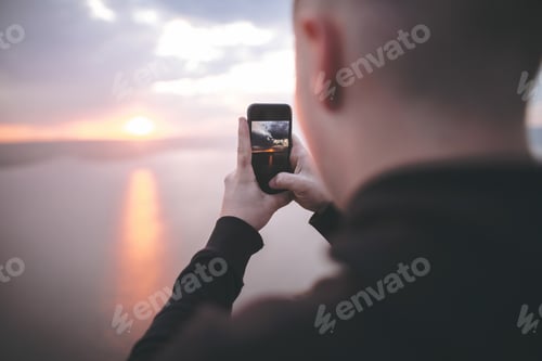 Preview: Hipster traveler taking photo on phone of amazing sunset view on river