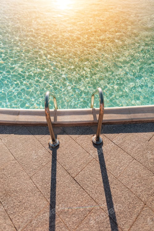 Preview: Beautiful swimming pool with azure blue water and metal descent at sunset, top view.