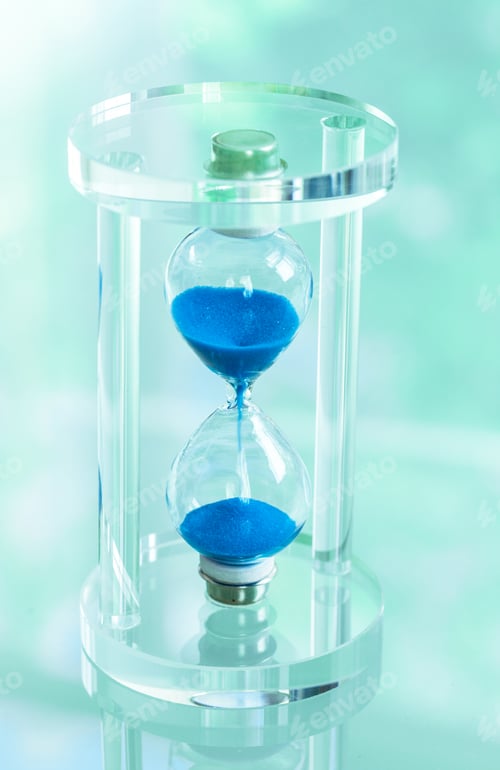 Preview: Hourglass with blue sand placed on a clear surface during a bright day