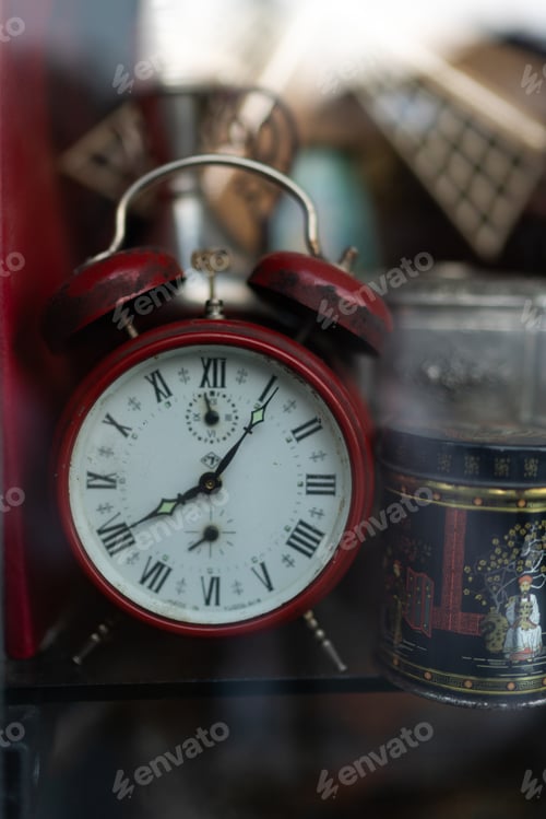 Preview: Old-school red twin bell alarm clock behind a shop window