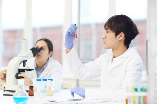 Preview: Asian lab employee looking at liquid in test tube