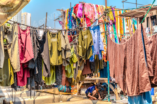 Preview: Kid playing under vibrant hanging clothes outdoors on a sunny day in Mumbai, India