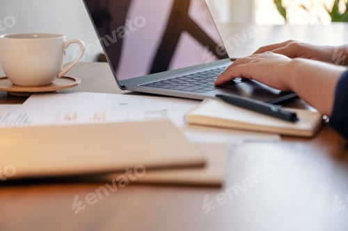 Preview: A woman using and typing on laptop with notebooks and papers on the table in office
